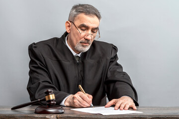 Judge signing the verdict. Judge's gavel on the table in the courtroom. Law Lord wearing gown using...