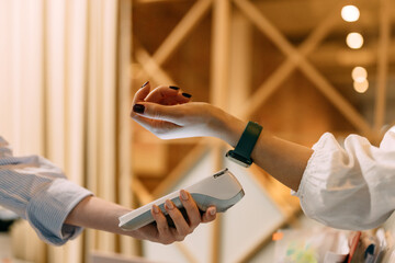 Side view of a female customer paying for her cost with a smart watch.