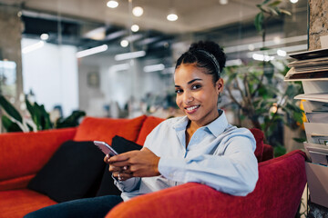 Fototapeta premium Portrait of a businesswoman sitting on the couch, holding a phone.