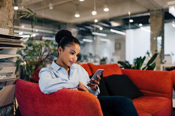 Pretty African woman browsing the internet on the couch at the workplace.