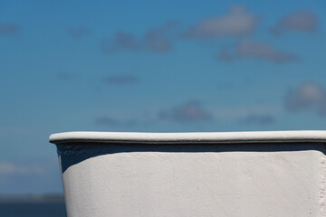 Close up side view of bow of a white ship hull against blue sky with white clouds