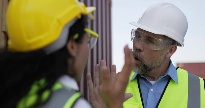 Pretty engineer female working on laptop computer, middle-aged Caucasian business manager man come in and blame the delay to loading Container in Shipping Port, logistics transportation concept.