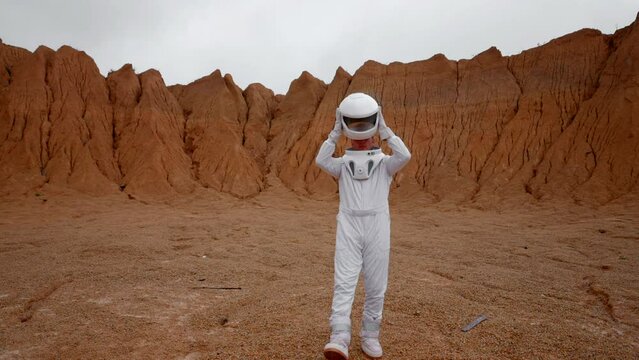Epic shot of an astronaut putting off cosmic helmet on red planet surface. Slow motion of caucasian man breathing in non-earth atmosphere with oxygen, good fur human life.