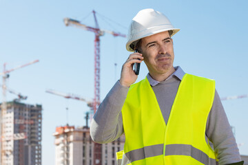 Professional builder standing talking on a phone in front of the construction site