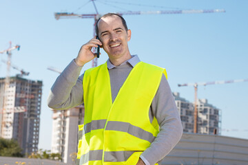 Professional builder standing talking on a phone in front of the construction site