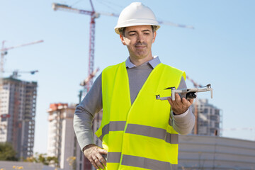 Man launches a quadcopter. An engineer flies a drone next to a construction site. Concept - construction observation with a drone.  Construction cranes on sunset sky
