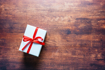 Eine weiße Geschenkbox mit roter Schleife auf einem braunen rustikalen Holz Tisch. Draufsicht.