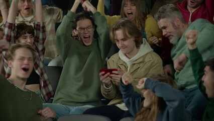 Audience sits at sports event, looking into the phone screen of a spectator instead of the game