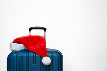 Blue plastic suitcase with Santa Claus hat over white background. Concept of travel and visit relatives on Christmas Holidays   