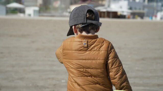 Back of child walking at beach wearing winter jacket and cap