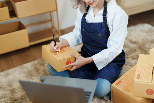 Starting small business entrepreneur of independent Asian woman smiling using computer laptop with cheerful success of online marketing package box items and SME delivery concept