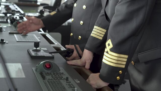 Ship's bridge. Officers stand at control panel. Hand turns joystick and hold radio. hief Mate, second mate patches on jackets.
