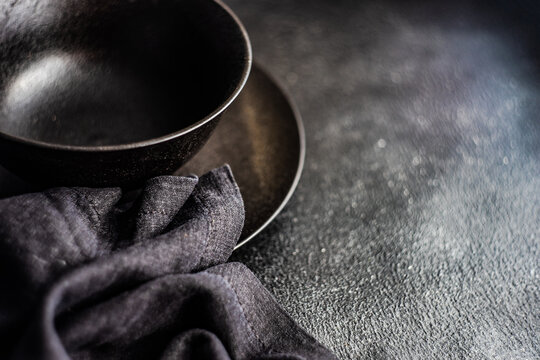 Close-Up Of A Black Ceramic Bowl, Plate And Napkin On A Black Table