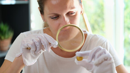 Female in white gloves holding magnifying glass and looking through at golden gem