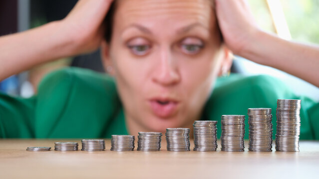 Shocked woman looking at piles of coins and holding on head