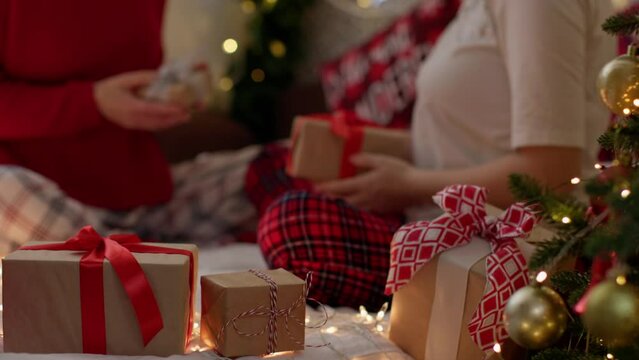 defocused couple in Christmas pajamas exchanging presents gift boxes with decorated Christmas tree and wrapped gifts on foreground. happy winter holidays concept morning boxing day family and friends