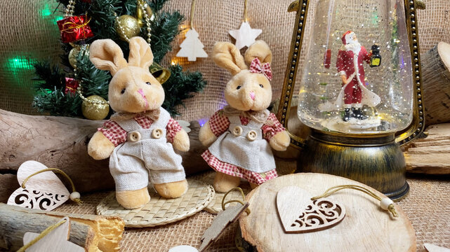 Couple of Christmas rabbits, 2023 animal, New Year tree and magical lantern with Santa Claus on wooden and burlap backgroundб folk style.  Selective focus.