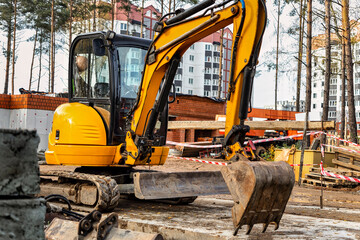 Close-up mini excavator during the construction of a modern residential complex. Miniature construction equipment for working in cramped conditions. - obrazy, fototapety, plakaty