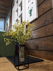 stylish decorative flowers in a modern vase on the table against the background of a wooden wall with a window