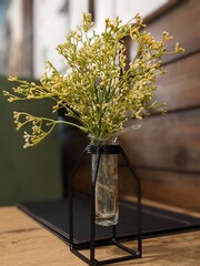 stylish decorative flowers in a modern vase on the table against the background of a wooden wall with a window