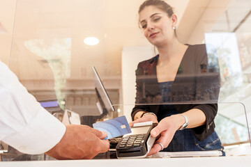 Una commessa alla cassa di un negozio  riceve il pagamento da parte di un cliente che paga con la...