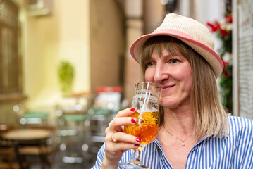 Woman in straw hat drinking beer on sidewalk cafe. Female tourist smiling enjoying the city life at a town square.