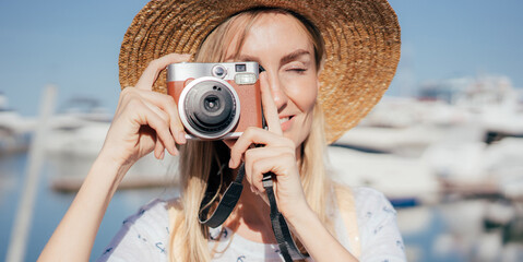 Happy young woman traveler photographer in straw hat taking photo on camera on sunny summer day.