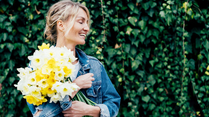 woman presses a bouquet of daffodils - obrazy, fototapety, plakaty