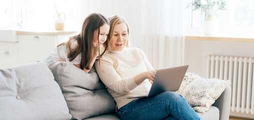 Mom and daughter spend time at home on the couch in the living room with a computer. Online...