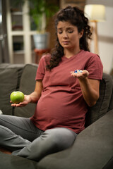 Pregnant woman choosing between pills and fruit..