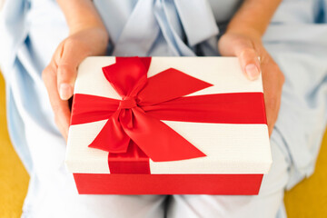 Woman hands holding beautiful giftbox with red bow. Festive red and white present box in woman's hands. Faceless image. Selective focus