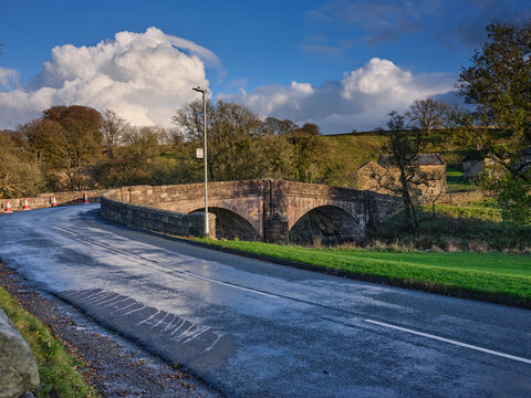 With white clouds looming in the background, looking southeast from the Slaidburn car park to the stone bridge over the River Hodder. Slaidburn