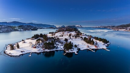 Aerial view of the snowy shoreline with rural houses against the background of the blue sky. Norway.