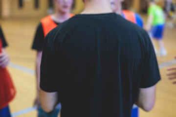 Junior young basketball team with a coach, group of kids children team having training and team talk speach with trainer instructor, basket coach explaining the game plan tactics on coach's clipboard