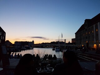 Sun setting behind the canal in the Copenhagen harbour while people are dining.