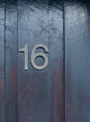 House number 16 (sixteen) in weathered metal on a dark-painted wood facade