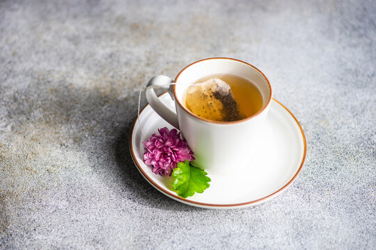 Cup Of Tea With Teabag Brewing And A Purple Chrysanthemum Flower On The Saucer