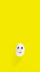 white egg with cheerful face on yellow background, vertical, 16:9