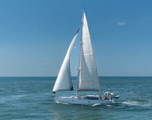 Naklejka premium A white yacht under sail on the ocean with three unidentified people on board.