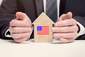 Businessman hand holding wooden home model with American flag. insurance and property concepts