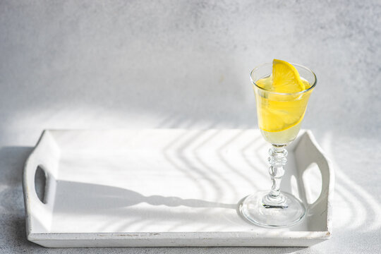 Glass of Limoncello with fresh lemon on a tray in the sunlight