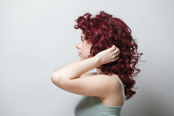Attractive woman touching her red curly hair against white wall background