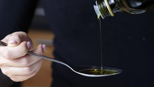 cook pours oil from bottle into tablespoon, close-up, glass bottle, dark background