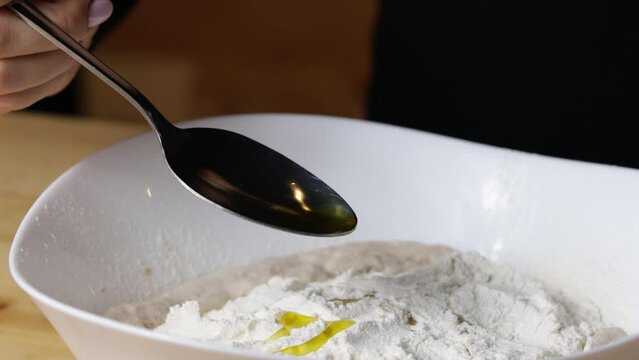 cook pours sunflower oil into tablespoon dough, close-up, pizza dough preparation