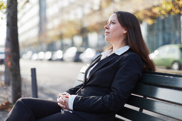 Businesswoman sitting relaxed on park bench in city and thinking