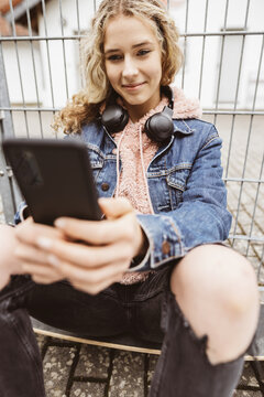 Young girl sitting on a skateboard with cell phone and surfing the internet