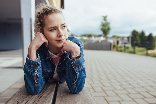 Young blonde thoughtful girl lying on wooden bench and looking to the side