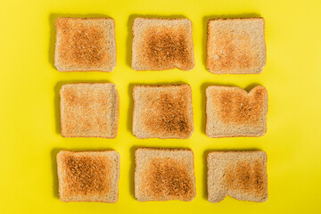 Top view of a pattern of several slices of toasted bread arranged on yellow background. Breakfast concept