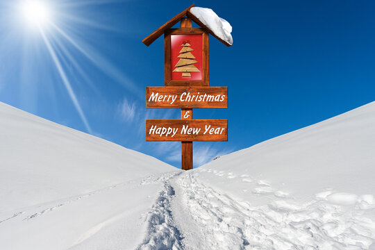 Merry Christmas and Happy New Year. Wooden Sign with a small Christmas tree with red comet star on a snowy landscape against a clear blue sky with clouds, sunbeams and copy space.