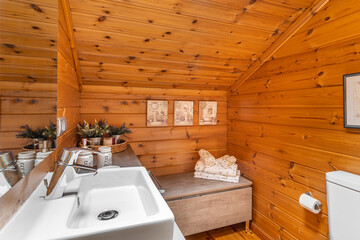 Cozy interior of bathroom in a country cottage with wooden walls. Sink, mirror and drawer with towels.